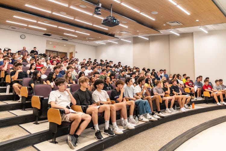 Students sit in an auditorium listening.