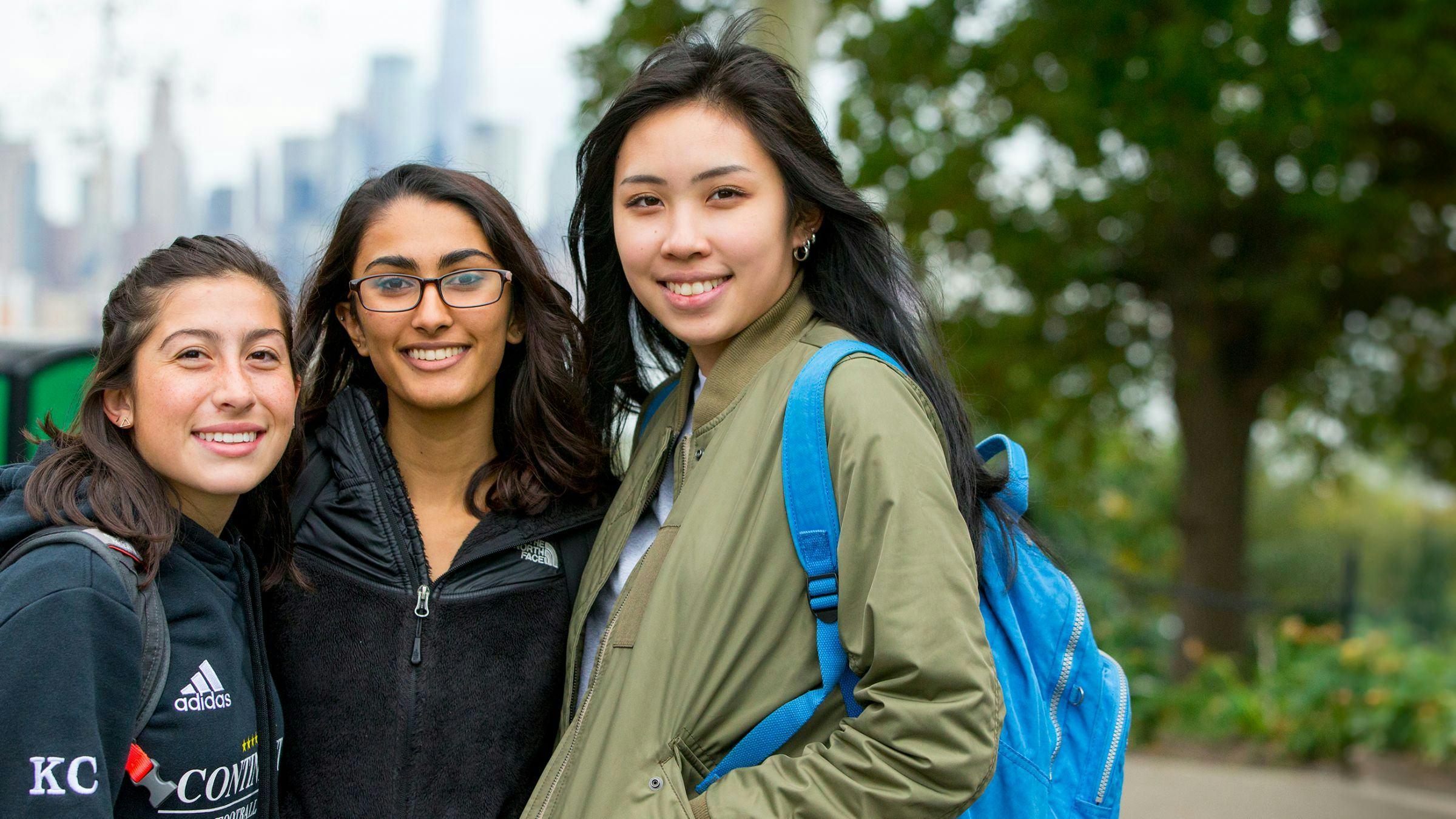 Three female students in the foreground with NYC skyline in the background
