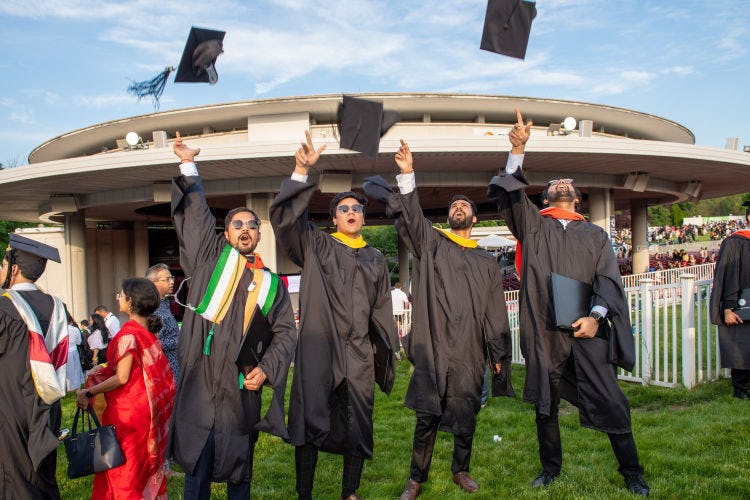 A group of graduates in regalia toss their caps