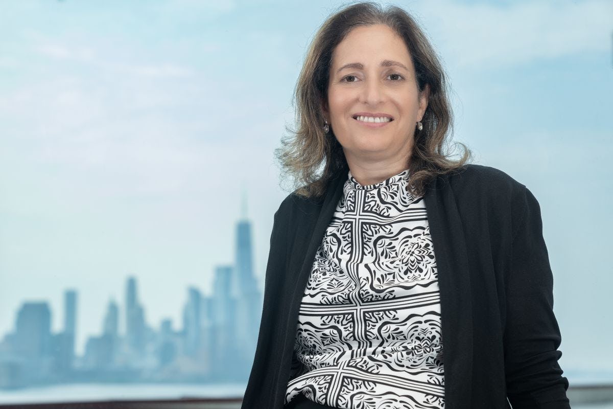 Dr. Joelle Saad-Lessler stands in front of a window with the New York City skyline in the background.