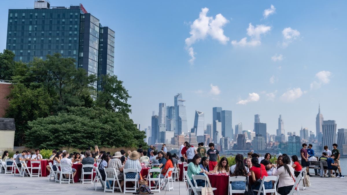 Students sitting at tables eating lunch with the New York City skyline in the background.