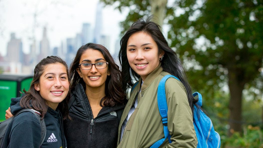 3 female students smiling with NYC skyline background
