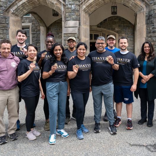 The EMBA cohort stands in front of the Thayer Hotel at West Point holding their Army coins.