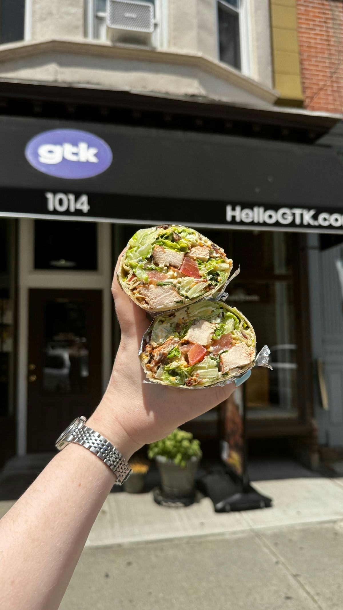 Hand holding two wraps in front of GTK storefront 