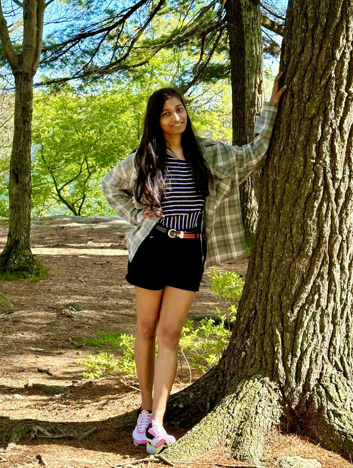 Photo of Shivani Bhawsar hiking in the woods, standing next to a tree