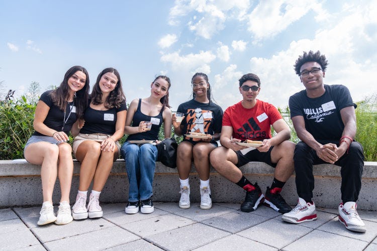 A group of students sit on the ledge surrounding the Babbio Center patio. 