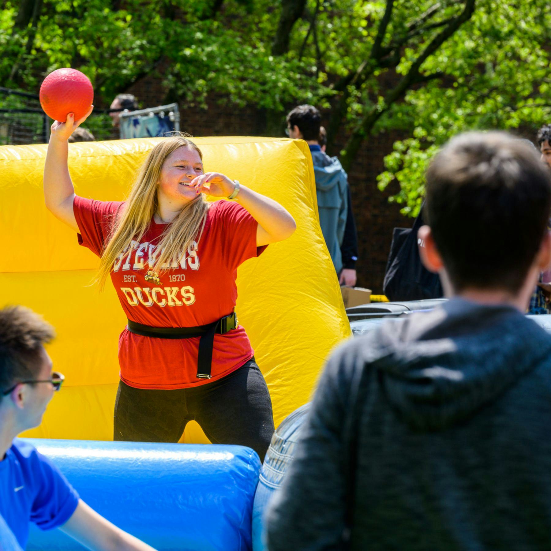 A woman throws a nerf ball while bouncing on an inflatable structure at Spirit Day 2023.