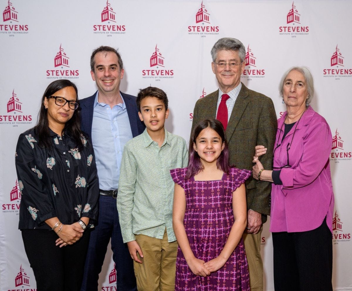 Bob Gilman standing with his wife, son and family in front of a Stevens-branded backdrop