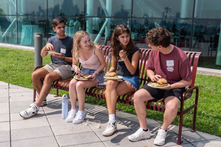 Students sit on a bench eating lunch on the Babbio patio. 