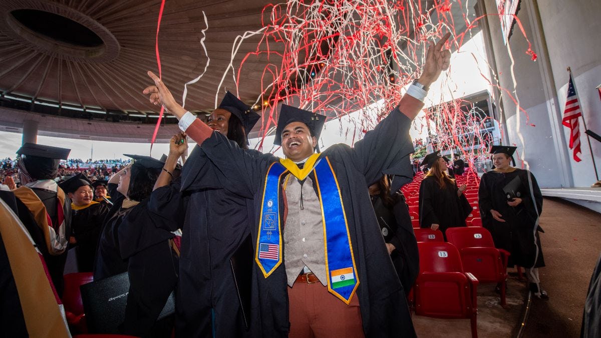 A graduate student celebrates his Commencement under a streams of read and gray confetti.