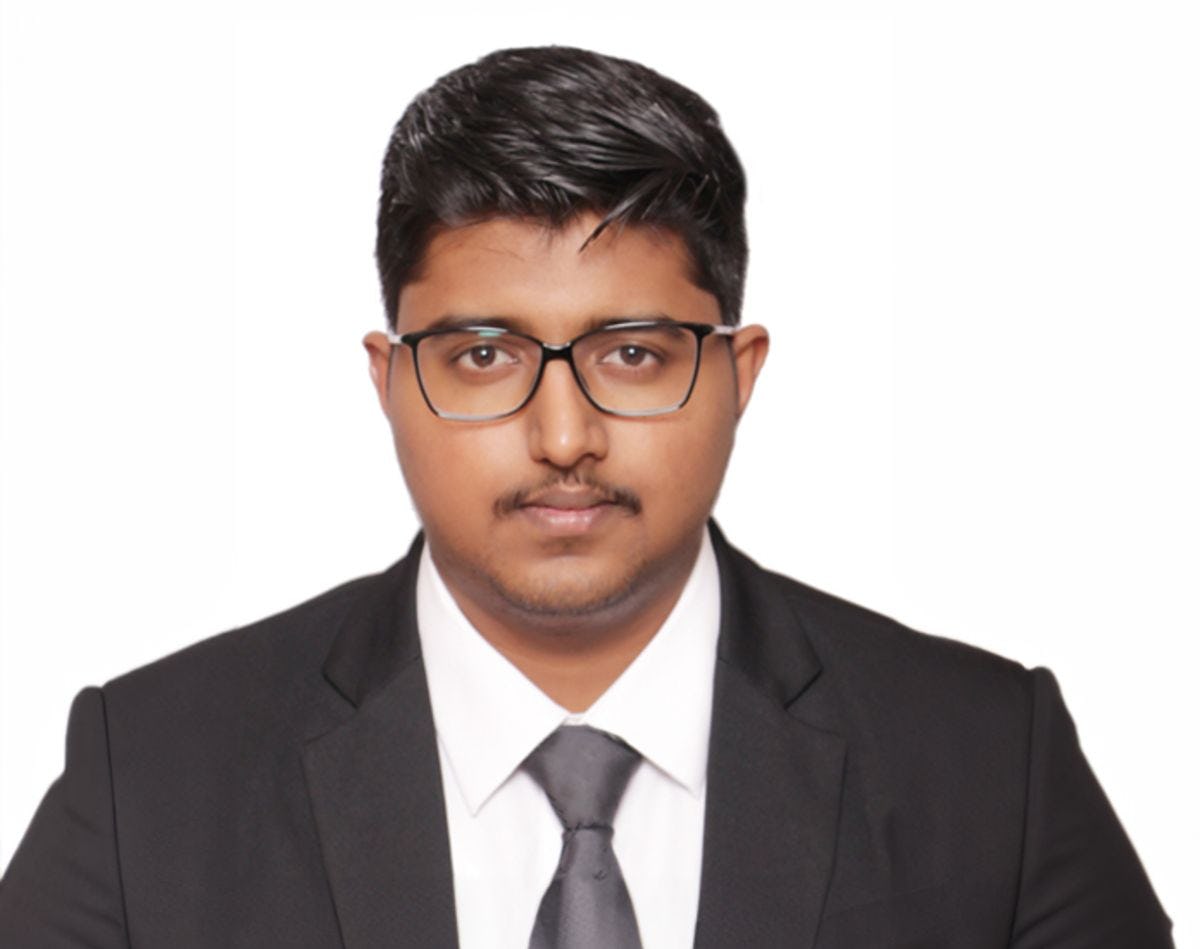 Tilak Chandana head and shoulders photo wearing a black suit, white shirt and dark gray tie.
