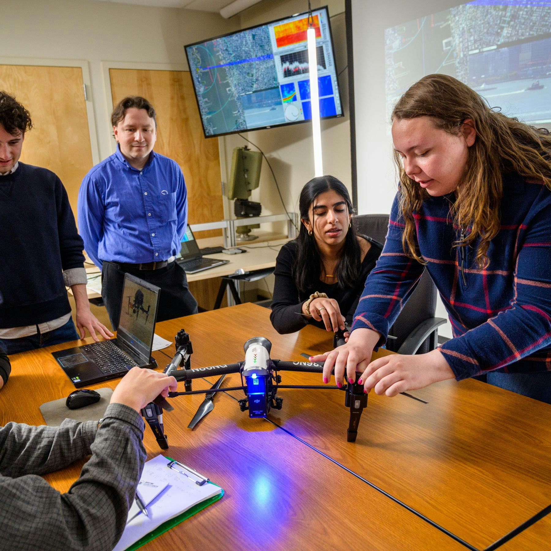 Students and professor adjust a drone in a classroom.