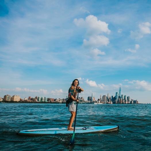 Jeremy Roche stand up paddle boarding on the Hudson River in front of the New York City skyline