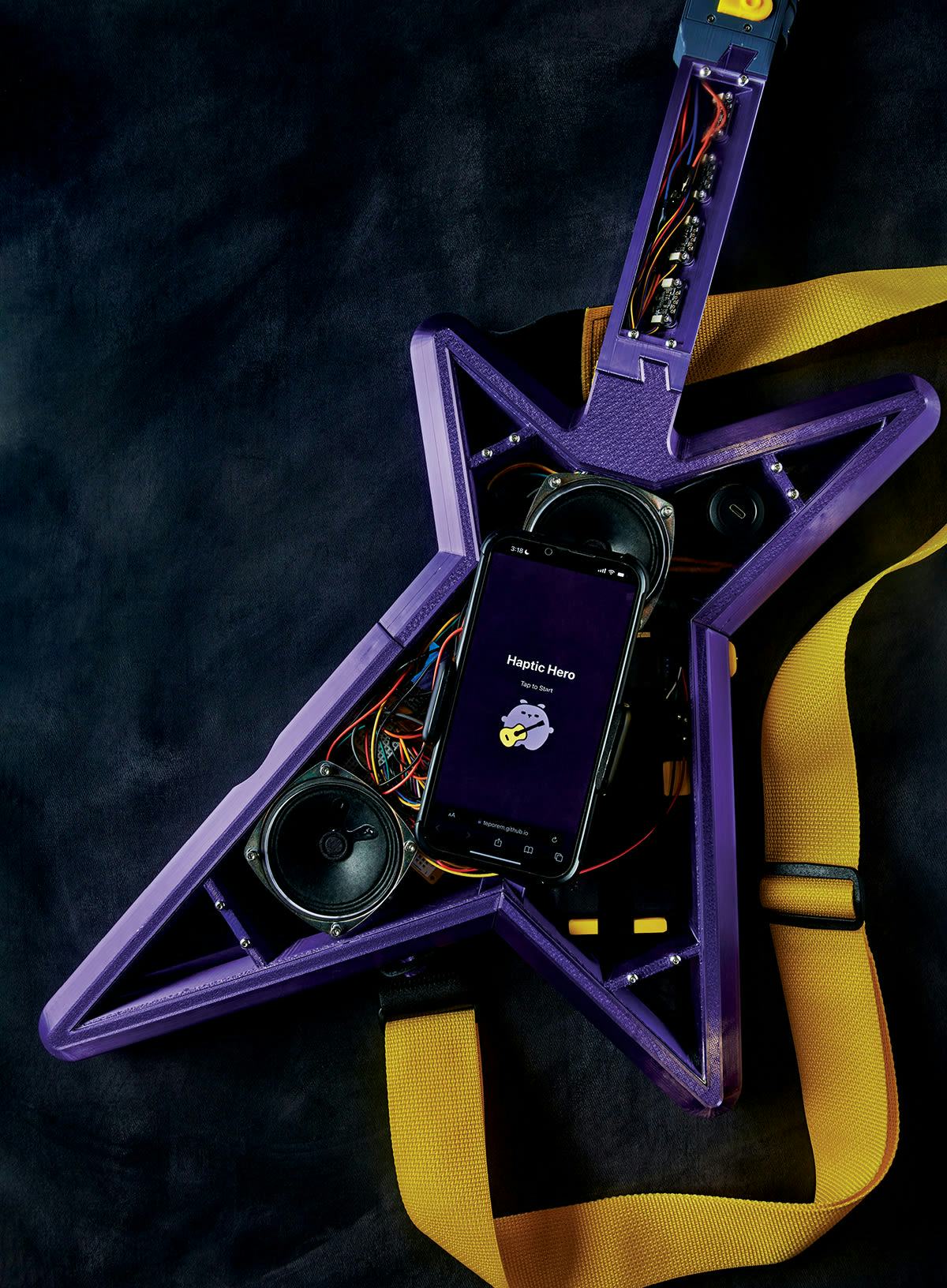 A close-up view of the Haptic Hero prototype, shaped like a real electric guitar. The face and neck of the purple guitar are open the electrical wiring and internal speaker are exposed. In the center of the guitar is an iPhone. 