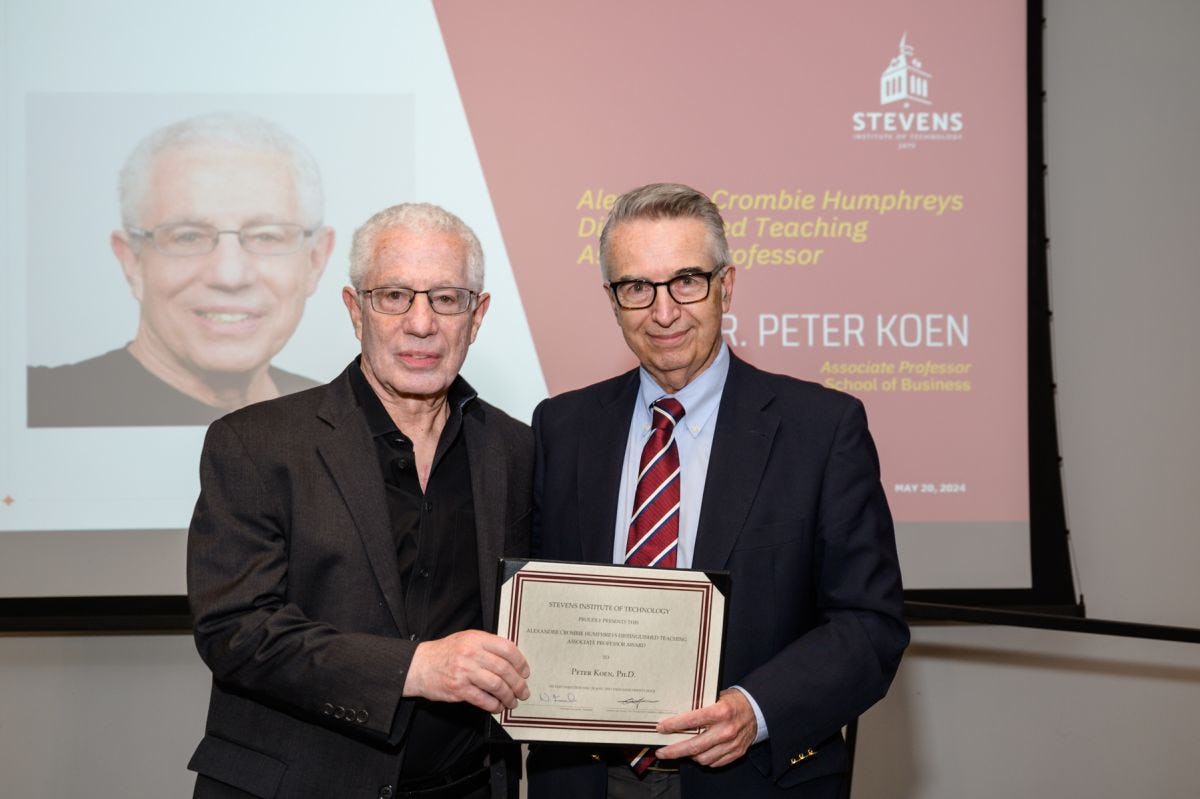 Peter Koen and Gregory Prastacos stand on the stage holding the award certificate. 