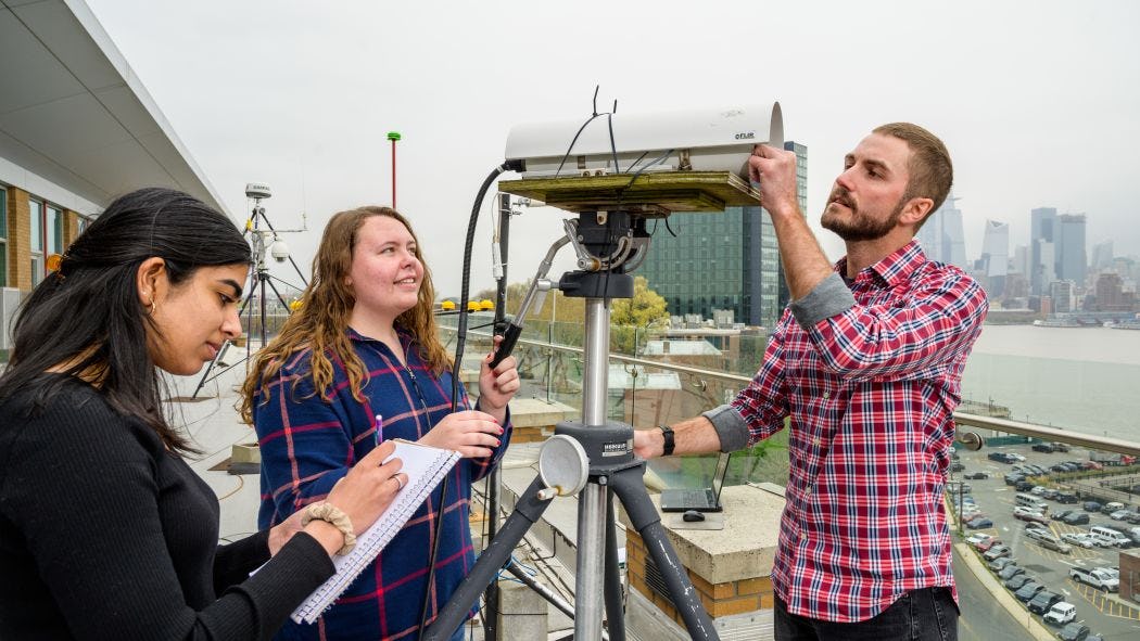Students on a roof work with a monitoring device.