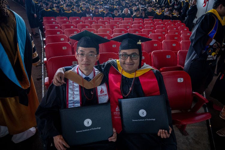 Two graduate students pose with diplomas 