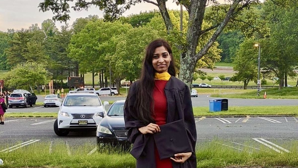 Student Shivani Bhawsar stands in a parking lot wearing her cap and gown for graduation