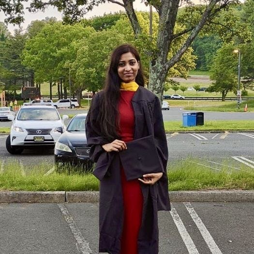 Student Shivani Bhawsar stands in a parking lot wearing her cap and gown for graduation