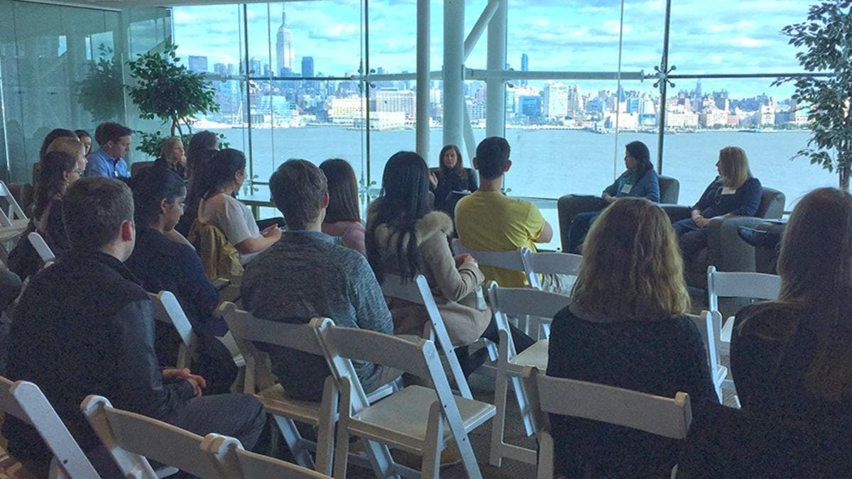 Panelists address a room packed with students in the Babbio Center at Stevens. The New York skyline is visible in the background.